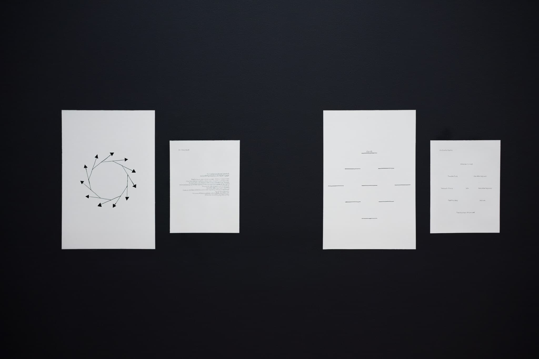 Four white sheets of paper display symbols and writings, cast against a black background.