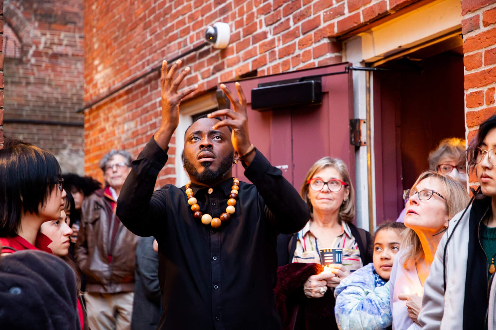 A performance artist looks at his raised hands in front of a crowd of people.